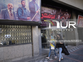 Two Iranian women wearing protective face masks walks past a closed cinema in northern Tehran following the new coronavirus (COVID-19) disea...