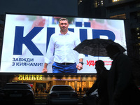 People walk next to a screen of a shopping mall that displays an election campaign advertisement of Kyiv mayor Vitali Klitschko in the cente...