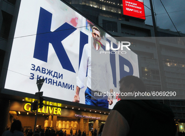 People walk next to a screen of a shopping mall that displays an election campaign advertisement of Kyiv mayor Vitali Klitschko in the cente...