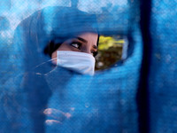 A Palestinian woman wearing a protective mask looks behind a curtain, on a street, amid the coronavirus disease (COVID-19) outbreak in Gaza...