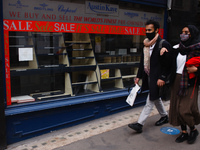 A man and woman wearing face masks walk past a closed-down watch shop on Bedford Street in London, England, on October 16, 2020. London is t...