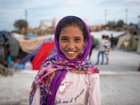 A smiling girl with a headscarf at the roof of a building where she lived after the fire. Portraits of young children refugees, minors boys...