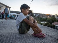 A refugee boy is staring from the roof of the building the new Karatepe refugee camp. Portraits of young children refugees, minors boys and...