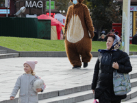 A woman with a child walk past an entertainer dressed in bear costume with the face mask on in downtown Kyiv, Ukraine, October 20, 2020. 173...