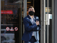 A man wearing a mask stands with electronic cigarette at the door of Roshen store downtown Kyiv, Ukraine, October 20, 2020. 173,788 active c...