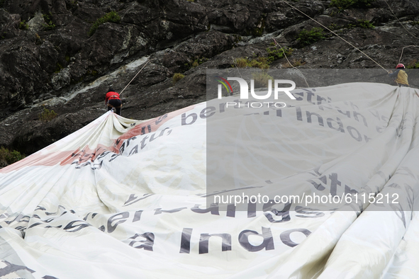 Two teenagers climbing a cliff to fly a large banner with the words Soempah Pemoeda on the Serelo Hill Cliff, Lahat Regency, South Sumatra P...