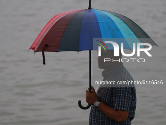 A man holds umbrella as he crosses over the Buriganga River by small wooden boats on a rainy day in Dhaka, Bangladesh on October 23, 2020....