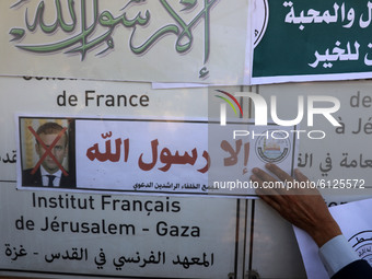 A Palestinian man puts up banners showing crossed out pictures of French President Emmanuel Macron during a protest against the publications...