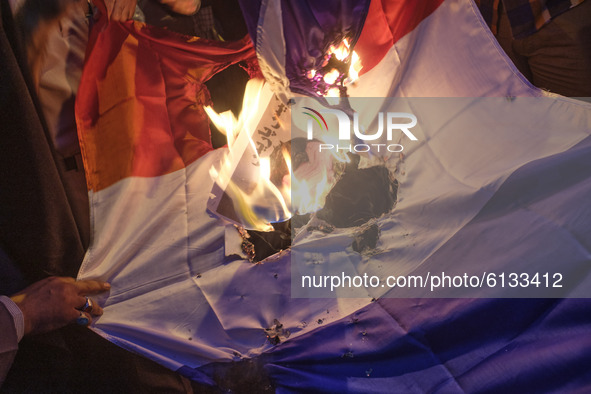 Iranian protesters burn a cartoon of the French President Emmanuel Macron and a French flag during a protest gathering in front of the Frenc...