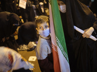 An Iranian schoolboy wearing a protective face mask holds an Iran flag during a protest gathering in front of the French embassy in Tehran o...