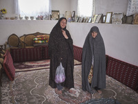 Two Iranian female villagers pose for a photograph as one of them holds a plastic bag loaded with Saffron crocus flowers as they stand in th...