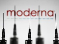 Medical syringes are seen with Moderna company logo displayed on a screen in the background in this illustration photo taken in Poland on No...