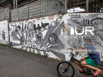 Child with bike and using mask passing by the mural. Mural about Covid19 at Bintaro South Tangerang, Banten, Indonesia. Indonesia have excee...
