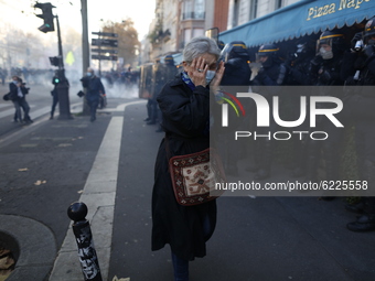A woman protects her face with her hands from gas in Paris on November 28, 2020 during a protest against the ''global security'' draft law,...