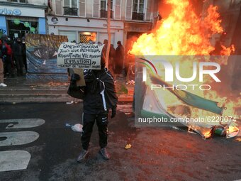 A man holding a sign poses in front a fire in Paris on November 28, 2020 during a demonstration to protest against the 