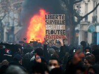A man holds a sign near a fire in Paris on November 28, 2020 during a demonstration to protest against the 