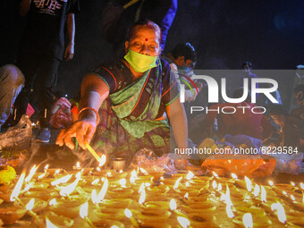 A lady wearing mask decorates a river bank with earthen lamps on the eve of Dev Deepawali . Dev Deepawali is a festival of Kartik purnima an...