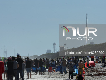 People watch from the beach at Canaveral National Seashore as a SpaceX Falcon 9 rocket with the Dragon spacecraft launches from pad 39A at t...