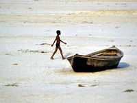 An indian boy walks as he passes by a boat on the sand  at dry river bed side of River Ganges,in Allahabad on June 8,2015..RIver Ganges shri...