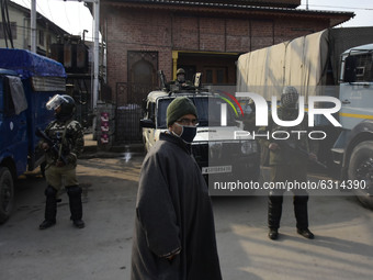 A Kashmiri masked man walks as Indian paramilitary troopers stand alert outside Jamia Mosque during shutdown against killing of three alledg...