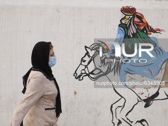 An Iranian woman wearing a protective face mask walks past a mural in western Tehran during a polluted air, following the COVID-19 outbreak...