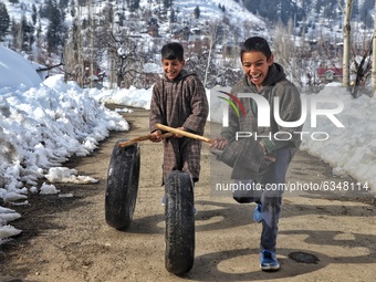 Kashmiri Kids playing with used vehicle Tyres in snow covered People walk in snow covered area of Hajibal on the outskirts of District Baram...