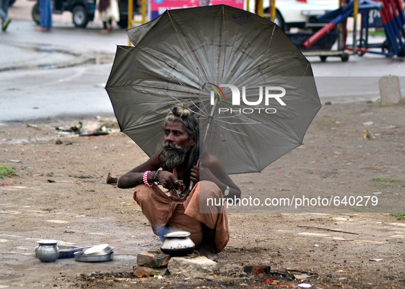 An indian sadhu holds umbrella as he cooks food on a temporary stove during fast blowing winds and rains,in Allahabad on June 15,2015. 