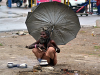 An indian sadhu holds umbrella as he cooks food on a temporary stove during fast blowing winds and rains,in Allahabad on June 15,2015. (