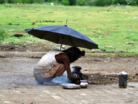 An indian sadhu holds umbrella as he cooks food on a temporary stove during fast blowing winds and rains,in Allahabad on June 15,2015. (