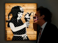 A member of staff poses with 'Girl With Ice Cream on Palette', by British artist Banksy, estimated at GBP300,000-500,000, during a press pre...