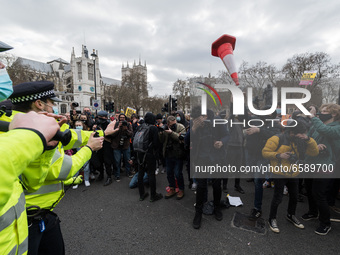 LONDON, UNITED KINGDOM - APRIL 03, 2021: Protester throws a traffic cone while a man wipes his eyes after police used pepper spray during a...