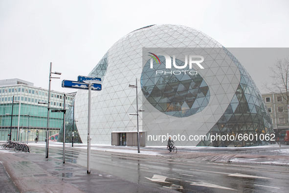 People walking and cycling their bikes in front of De Blob, a modern architecture building, during the snowfall. The third day of the unusua...
