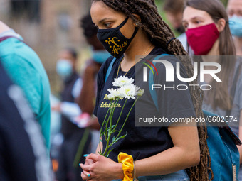 A woman holding a flower listens to a speaker address the crowd as people gather at Washington Park in memorial and then march to where Timo...