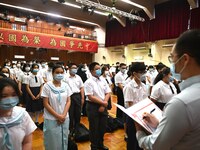A teacher takes attendance as students wearing face masks stand and watch, while standing under a banner with patriotic slogans, during a fl...