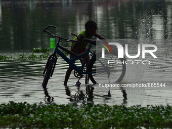 An inndian boy washes his bicycle  by blocked  rain water in a flooded pathway following heavy rain in Allahabad on July 1,2015. (