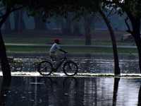 An indian young cricketer rides his bicycle as he moves towards his playground, in a flooded pathway following heavy rain in Allahabad on Ju...