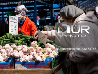 A woman in protective face mask browse through fresh spring green vegetable at outdoor market in central Krakow, Poland on May 6, 2021. (