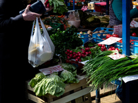 A woman in protective face mask browse through fresh spring green vegetable at outdoor market in central Krakow, Poland on May 6, 2021. (