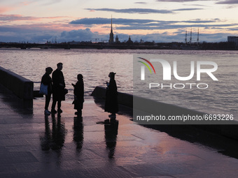 People walk along the embankment of the Neva River. Storm clouds hang over the Peter and Paul Fortress in St. Petersburg, Russia. (