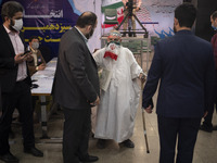 An unidentified elderly man covers his face with an Iran flag instead of protective face mask looks on while attending the election headquar...