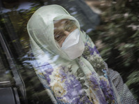 An Iranian elderly woman wearing a protective face mask looks on as she sits in a vehicle while waiting to receive a dose of the new coronav...