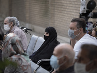 An Iranian elderly woman wearing a protective face mask sits in an outdoor area while waiting to receive a dose of the new coronavirus disea...