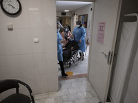 An Iranian medical personnel wearing a protective suit carrying an elderly woman by a wheelchair for receiving a dose of the China's Sinopha...