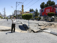A Palestinian man take pictures with his smart phone of a huge crater on a main road in Gaza City on May 13, 2021, following continued Israe...