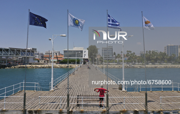A man towels off after swimming on a pier with flags of the EU, Limassol, Greece and Cyprus in the Mediterranean port of Limassol. Cyprus, T...