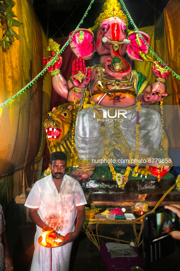 Tamil Hindu priest performs prayers by a large clay idol of Lord Ganesha (Lord Ganesh) at a pandal (temporary shrine) along the roadside dur...