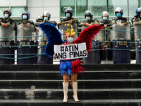 A protester in Philippine flag-inspired dress holds a placard with the text 