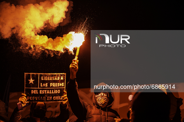 A person holds a flare, next to a sign with the phrase -Free the prisoners of the popular uprising in Chile-.  
In the middle of the demons...