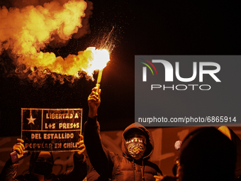 A person holds a flare, next to a sign with the phrase -Free the prisoners of the popular uprising in Chile-.  
In the middle of the demons...