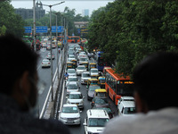 People take cover from rain on a foot over bridge as they watch vehicles plying  amid dense traffic after heavy rains in New Delhi, India on...